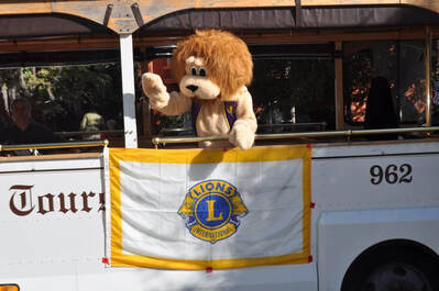 Picture of a parade bus with the Lions Flag and a person dressed in a Lions suit waving to the crowd.